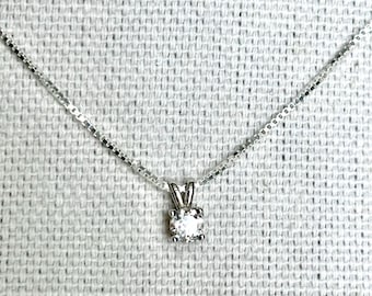 May include: A silver chain necklace with a small, clear, round gemstone pendant.