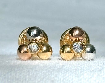 Può includere: Un paio di orecchini d'oro, ognuno con tre sfere rotonde in diverse tonalità di oro: bianco, giallo e rosa. Un piccolo diamante è incastonato al centro di ogni orecchino.