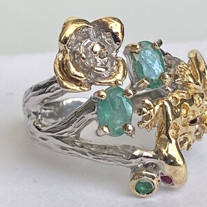 May include: A silver ring with a gold lizard, a gold flower, and green gemstones. The ring is designed to look like a branch.