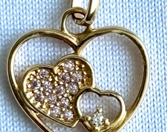 Könnte beinhalten: Ein goldener herzförmiger Anhänger mit drei kleineren Herzen darin. Das größte Herz ist in Gold umrandet und die beiden kleineren Herzen sind mit kleinen rosa Steinen gefüllt. Das kleinste Herz hat einen einzigen klaren Stein in der Mitte.