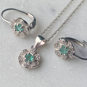 Op de afbeelding: Een zilveren ketting en oorbellen set met een groene edelsteen omringd door kleinere witte edelstenen.