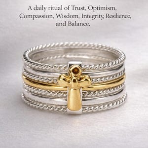 May include: A stack of silver rings with a gold cross-shaped charm. The rings have a twisted rope design on the edges. The image includes the text "Seven Virtues, One Soul."
