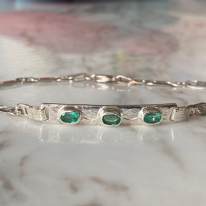 Puede incluir: Una pulsera de plata con un diseño de cadena de eslabones y una barra rectangular con tres piedras preciosas verdes ovaladas.
