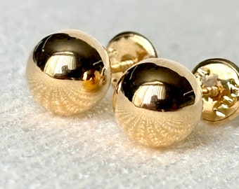 Può includere: Un paio di orecchini a lobo a forma di sfera dorata con una superficie liscia e riflettente. Ogni orecchino presenta un design sferico con una chiusura a perno sicura, mostrando una finitura giallo metallizzato brillante e lucida.