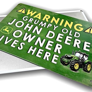 May include: A green metal sign with the text "WARNING GRUMPY OLD JOHN DEERE OWNER LIVES HERE" and a John Deere tractor graphic. The sign has a distressed look and is mounted on a silver metal backing.