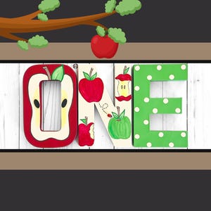 May include: Three decorative wooden letters spelling the word ONE. The O is shaped like a sliced apple, the N features painted red and green apples with a ladybug, and the E is green with white polka dots. The letters are arranged horizontally.