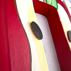 May include: A wooden wall-mounted coat rack featuring a series of painted red apple motifs on a cream-colored background. The rack includes dark brown circular hooks attached to the front, with each apple design accented by green leaves and brown stems.
