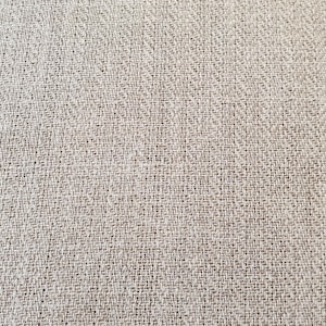 May include: Close-up of a beige woven fabric with a subtle texture. The fabric has a fine weave and a slightly rough surface.