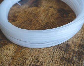 Può includere: Una bobina continua di cordino in plastica bianca traslucida avvolta in forma circolare. Il cordino presenta un profilo liscio e arrotondato con una consistenza semi-flessibile, formando molteplici anelli concentrici sovrapposti.