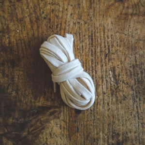 May include: A close-up of a white cotton shoelace rolled up on a wooden surface.