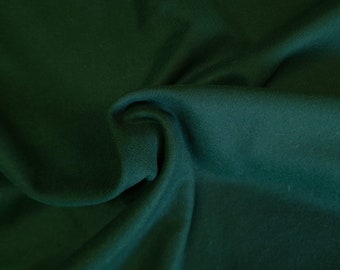 May include: Close-up of a dark green fabric with a soft, textured surface. The material is draped and folded, creating shadows and highlights that emphasize its texture. The fabric appears to be a solid color, suitable for various sewing projects.