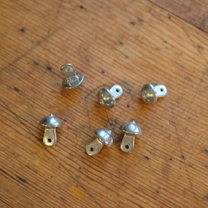 May include: A set of six silver-toned metal furniture feet with a rounded top and a flat base. The feet are designed to be attached to the bottom of furniture legs.