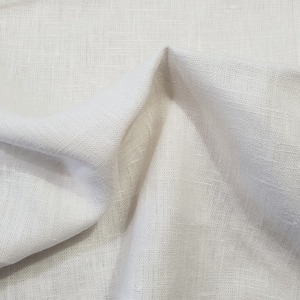 May include: A close-up of a white linen fabric with a textured weave. The fabric is folded and draped, showing its soft and natural texture.