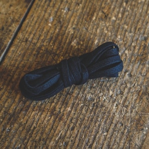May include: A black elastic shoelace, coiled and ready to be used.
