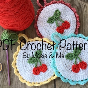 Puede incluir: Patrón de crochet PDF para un conjunto de tres agarraderas con temática de cereza. Las agarraderas son blancas con un borde amarillo, turquesa y rojo. Cada agarradera presenta una cereza roja con un tallo y hojas verdes.