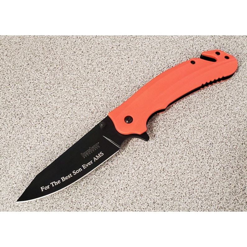 May include: A black folding knife with an orange handle. The blade is engraved with the text "For The Best Son Ever AMS".