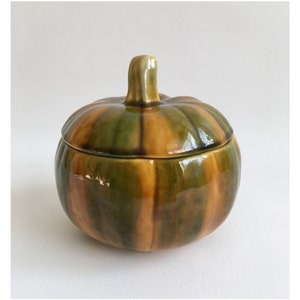 以下が含まれることがあります： 蓋付きのセラミック製かぼちゃ型の容器。容器は緑、茶色、黄色の色合いで釉薬がかけられています。
