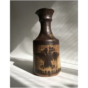 May include: A brown ceramic pitcher with a wide base and a narrow neck. The pitcher has a mottled glaze with brown and tan colors.