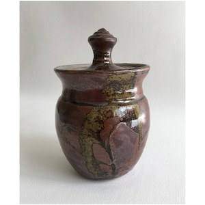 May include: A brown ceramic jar with a lid. The jar has a mottled glaze with brown, green, and black accents. The lid has a knob on top.