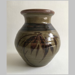 May include: A brown ceramic vase with a wide base and a narrow neck. The vase has a brown and black glaze with a design of stylized leaves.