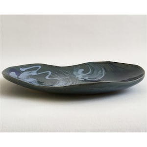 May include: A dark gray ceramic serving dish with a wavy, organic shape. The dish has a blue and white glaze with abstract designs.