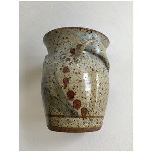 May include: A speckled brown and gray ceramic vase with a unique handle. The vase has a speckled glaze with brown spots.