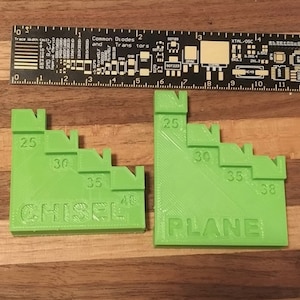 May include: Two green plastic woodworking tools with graduated markings. The tool on the left is labelled "CHISEL" and has markings of 25, 30, 35, and 40. The tool on the right is labelled "PLANE" and has markings of 25, 30, 35, and 38.