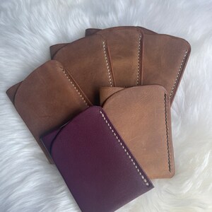 May include: Five brown leather card holders with white stitching, and one purple leather card holder with white stitching.