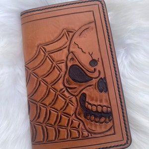 May include: A brown leather wallet with a tooled design of a skull and spider web.