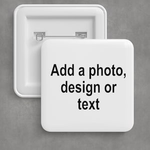 May include: Two white square pinback buttons. One button is face up, displaying the text "Add a photo, design or text" in black. The other button is face down, showing the pin and clasp. The background is a neutral gray.