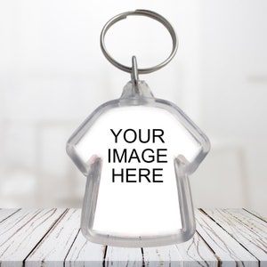 May include: Clear plastic keychain in the shape of a shirt with a silver key ring. The text "YOUR IMAGE HERE" is printed in black on the white shirt-shaped insert. The keychain is displayed on a white wooden surface.