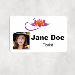 May include: A white name tag with a photo of a woman wearing a hat. The name tag has the name "Jane Doe" in bold black font, with "Florist" below. A lotus flower logo is at the top.