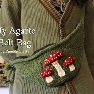 Könnte beinhalten: Eine grüne gehäkelte Gürteltasche mit Reißverschluss und einem Design aus roten und weißen Pilzen. Die Tasche wird von einer Person getragen, die einen grünen Pullover mit braunen Streifen trägt.