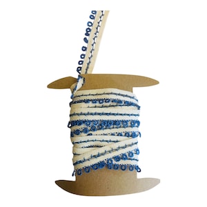 May include: A spool of white trim with blue trim and blue beads. The trim is wound around a cardboard spool.