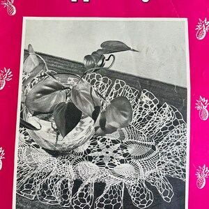 May include: A vintage crochet pattern book cover featuring a black and white photo of a crocheted doily with a plant in a glass vase. The cover is pink with the title "Pineapple Pageant" and the text "FEATURING RUFFLED DOILIES".
