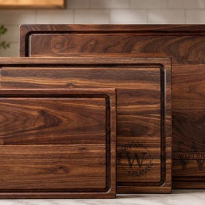 May include: A set of three rectangular dark brown walnut wood cutting boards of varying sizes, each featuring a deep juice groove along the perimeter. The two larger boards are engraved with a letter W and the name WITTEK in a decorative style.