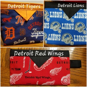 May include: Three fabric bags with different Detroit sports team logos. The top left bag is blue with orange trim and the Detroit Tigers logo. The top right bag is blue with black trim and the Detroit Lions logo. The bottom bag is red with black trim and the Detroit Red Wings logo.