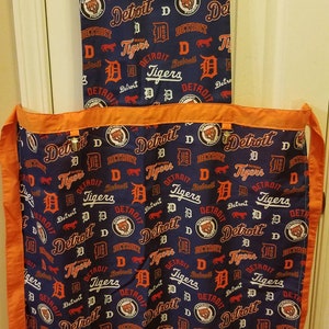 May include: A blue and orange kitchen apron with a repeating pattern of the Detroit Tigers logo, the word "Detroit", and the letter "D".