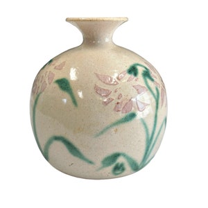 Puede incluir: Un jarrón de cerámica blanca con cuerpo redondo y cuello estrecho. El jarrón está decorado con diseños florales rosas y verdes.