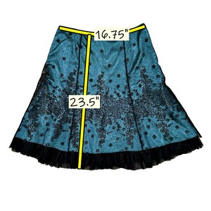 Op de afbeelding: Een turquoise rok met zwarte kanten overlay en een gefranjerde zoom. De rok is 59,7 cm lang en 42,5 cm breed in de taille. Het kant heeft een bloemenmotief.