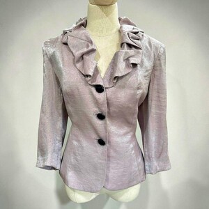 K&ouml;nnte beinhalten: Ein helllila Blazer mit ger&uuml;schtem Kragen und drei schwarzen Kn&ouml;pfen. Der Blazer hat Dreiviertel&auml;rmel und einen leicht strukturierten Stoff. Das Kleidungsst&uuml;ck wird auf einer Schaufensterpuppe pr&auml;sentiert.