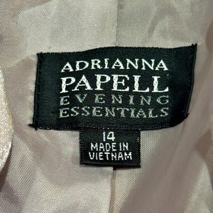 K&ouml;nnte beinhalten: Nahaufnahme eines schwarzen Etiketts mit wei&szlig;em Text, der "ADRIANNA PAPELL EVENING ESSENTIALS" lautet. Darunter befindet sich ein kleineres Etikett mit der Aufschrift "14 MADE IN VIETNAM".