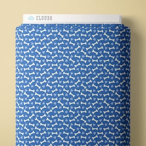 Könnte beinhalten: Eine Rolle blauen Stoffes mit einem sich wiederholenden Muster aus weißen Hundeknochen und hellblauen Herzen. Der Stoff ist mit "CLOUD9" in weißer Schrift auf weißem Hintergrund beschriftet.