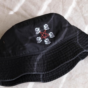 May include: A black bucket hat featuring an embroidered design of five small white computer monitors arranged in a circle, connected by a thin red pentagram line stitched in the center of the front panel of the hat.