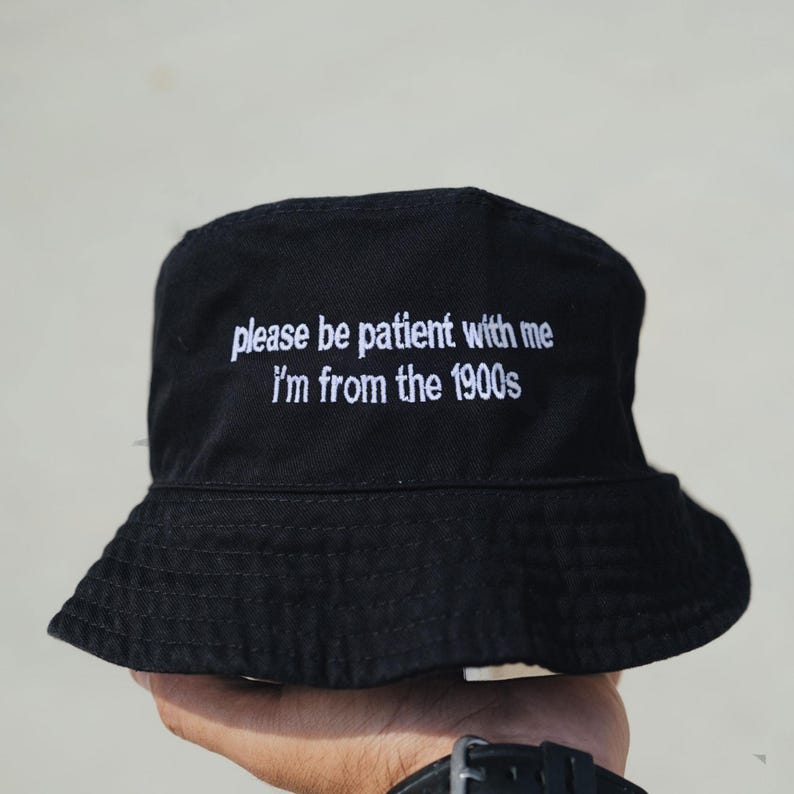 Peut inclure: Chapeau bob noir avec inscription brod&eacute;e en blanc "please be patient with me i'm from the 1900s"