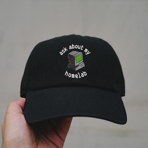 Può includere: Cappellino da baseball nero con la scritta ricamata "ask about my homelab" sopra una grafica di computer retrò con schermo verde. Il cappellino ha una visiera curva e una chiusura regolabile.