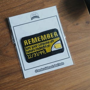May include: A black and yellow embroidered patch with the text "REMEMBER" and "Turn your computer off before midnight on 12/31/99." The patch is on a white card with a hat logo and the Instagram handle @embroidered.dad.hats.