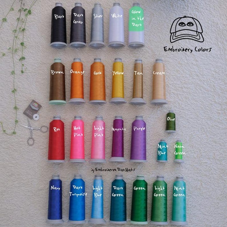 Pu&ograve; includere: Una collezione di rocchetti di filo da ricamo colorati in varie tonalit&agrave;, tra cui nero, grigio, argento, bianco e fosforescente. L'immagine presenta anche una grafica di cappello e il testo "Embroidery Colors."