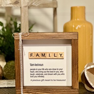 Può includere: Un cartello di legno con la parola "FAMILY" scritta con tessere da Scrabble. La definizione di famiglia è scritta sotto le tessere: "am-lee
oun people in your life who are close to your heart, who bring out the best in you, who laugh, celebrate, and dream with you, who love you infinitely. A precious gift meant to be treasured"