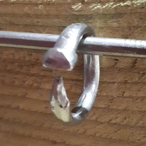 May include: A silver metal ring with a unique design, featuring a pointed end and a rounded top. The ring is made of a single piece of metal and has a smooth, polished finish.